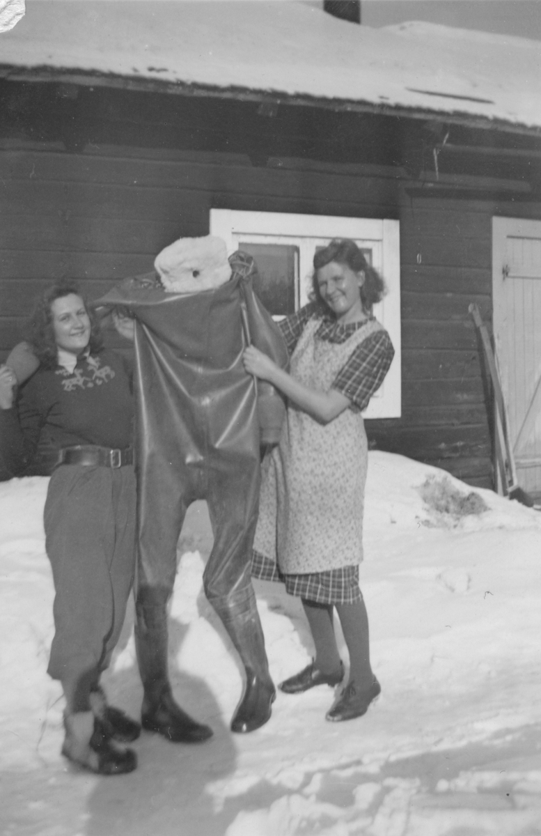 Två kvinnor håller upp en våtdräkt, vintertid, 1942. Birgit Johansson till vänster är luftbevakare, kvinnan till höger en okänd kvinna. Birgit tillhörde 91:a ls-kompaniet i Tellejåkk, Kåbdalis under beredskapsåren.