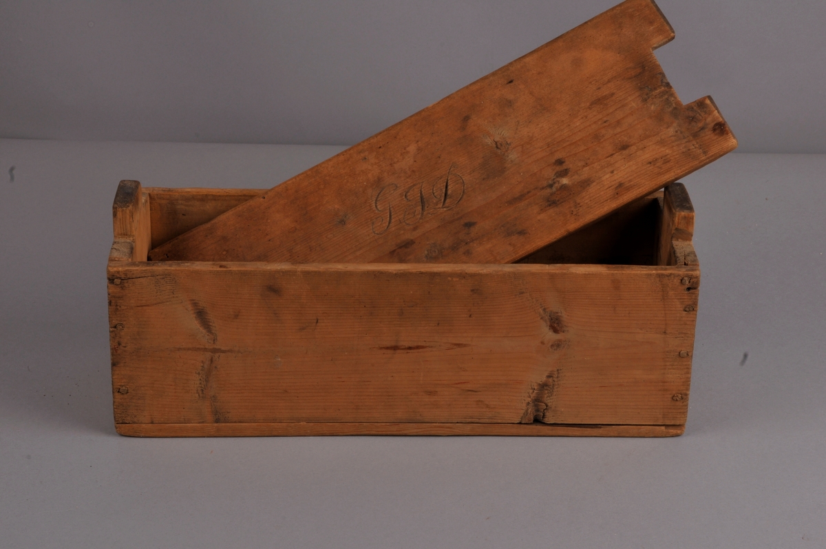 Rektangulær kasse med lok, nagla saman med trenaglar, lok med innskorne initsialar.