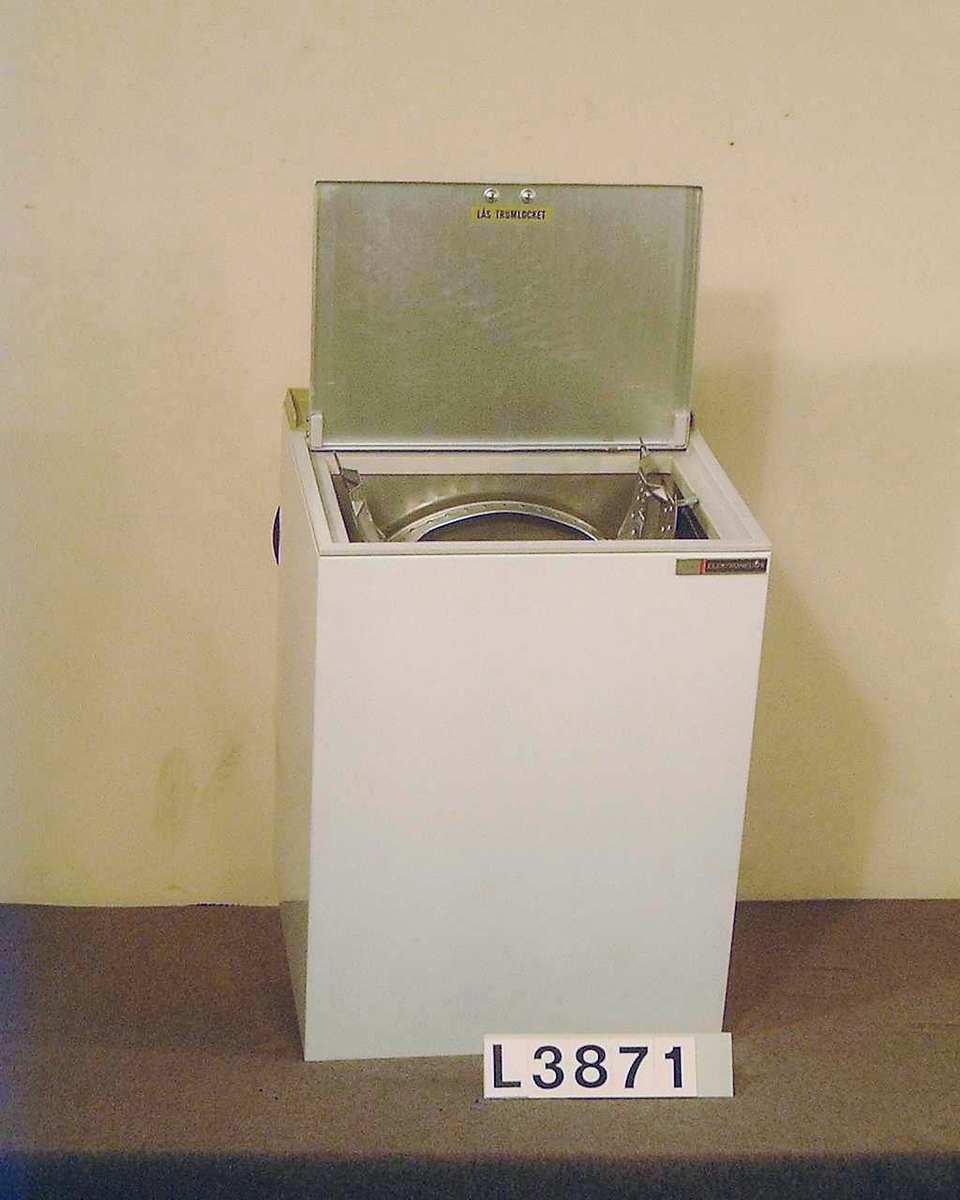 Toppmatad delautomatisk tvättmaskin, maskinen centrifugerar inte. Maskinen är vitlakerad, grå-grön instrumentpanel.  3 st blanka vred samt signallampa. Maskinen kan rullas. Bruksanvisning(kopia) ligger i tvättcylindern. Avloppsslangen har delvis torkat.