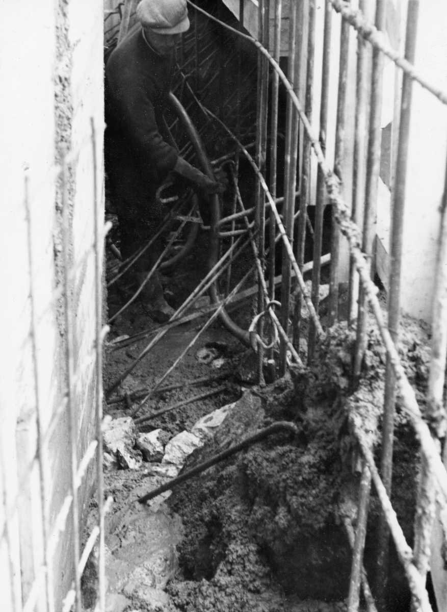 Ståpearbeid i forbindelse med bygging av kai for Glomma fellesfløtingsforenings båter i nedre del av vassdraget ved Furuholmen i Varteig i 1953.  Fotografiet er tatt inni forskalinga, antakelig i det som skulle bli den nedre delen av muren.  Vi ser at det er plassert et ståltrådbundet nettverk av forholdsvis grovt armeringsstål inntil den ene veggen i forskalinga, mens det er brukt et spinklere, forhåndssveiset armeringsnett på den andre.  Et par meter framfor fotografen ser vi en arbeidskledd mann med sixpencelue på hodet som håndterer en slange som sikkes ned i den flytende betongen.  Under en kopi av fotografiet i Glomma fellesfløtingsforenings album nr. 50 har noen skrevet følgende kommentar til motivet: «Vibratoren gjorde godt arbeid».