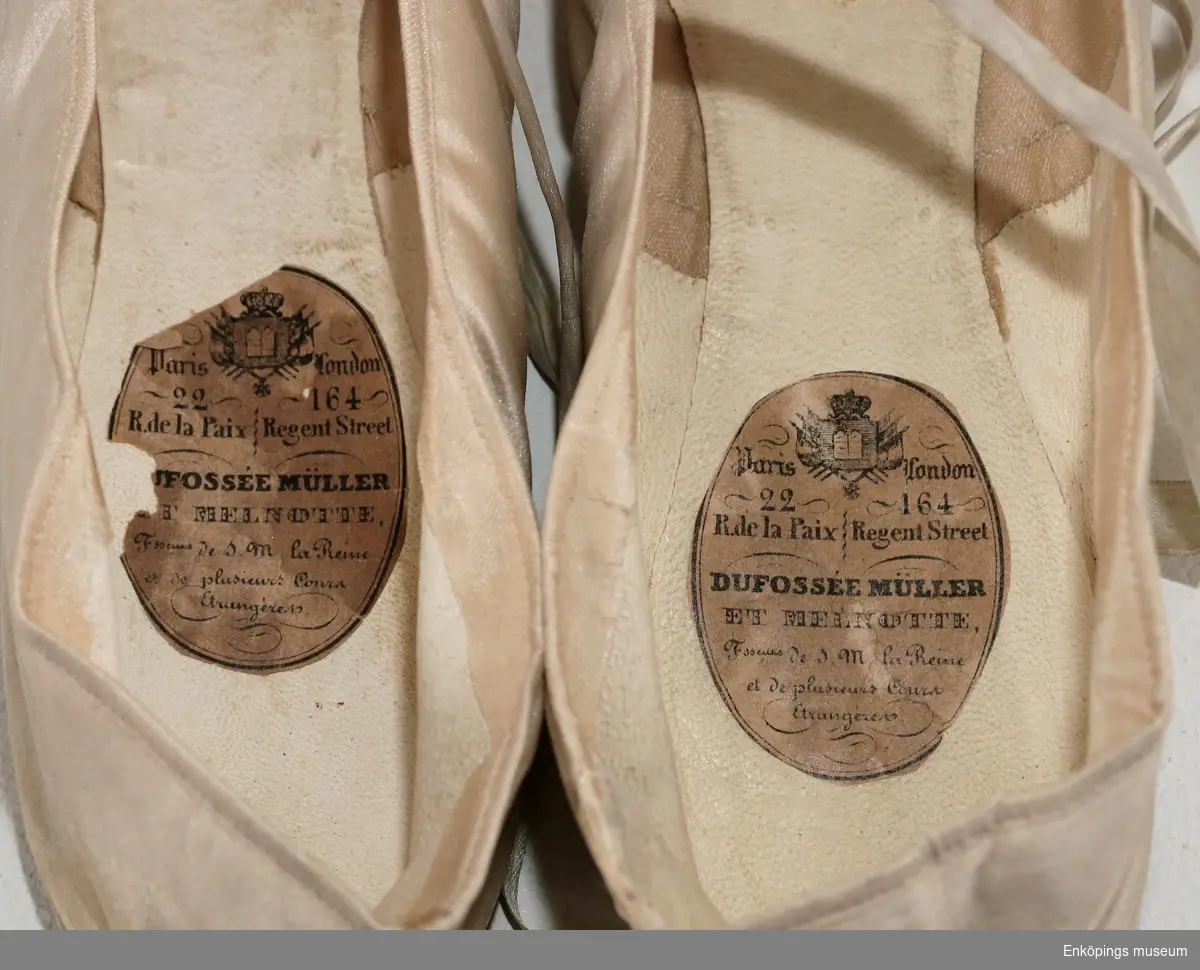 Cremefärgade balettskor med skinnfoder. Försedd med sidenband för att kunna knyta skorna runt vristen och en liten sidenblomma som dekoration. 
Tillverkare: Dufossée Müller et Melnotte, Paris, Frankrike.
Troligtvis från mitten av 1800-talet.