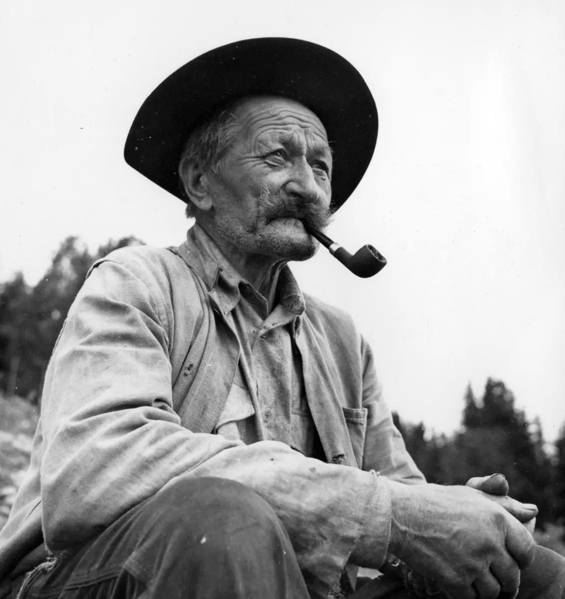 Otto Tyskeberget sitter med pipa i munnen og med hatt på hodet