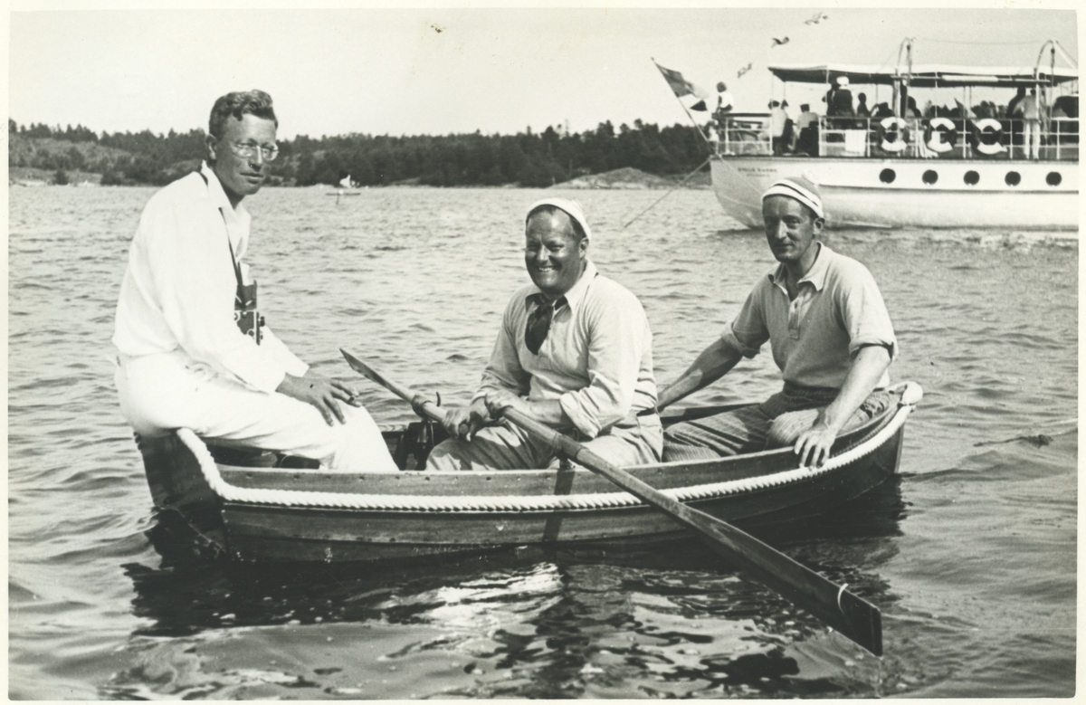 Tre män i en båt under KSSS:s långfärdssegling genom Södermanlands och Östergötlands skärgårdar i juli 1932. I mitten Gunnar Rooth, i aktern David Öhman, i fören oidentifierad person, i bakgrunden Erik Åkerlunds motoryacht STELLA MARINA.