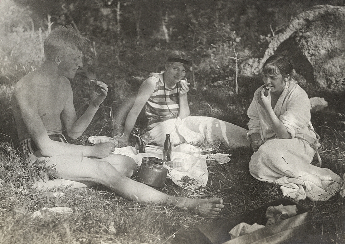 Två unga kvinnor och en dito man som äter lunch i det fria.
Text vid fotot: " - Ibland tilläts - flickorna följa med - ".
