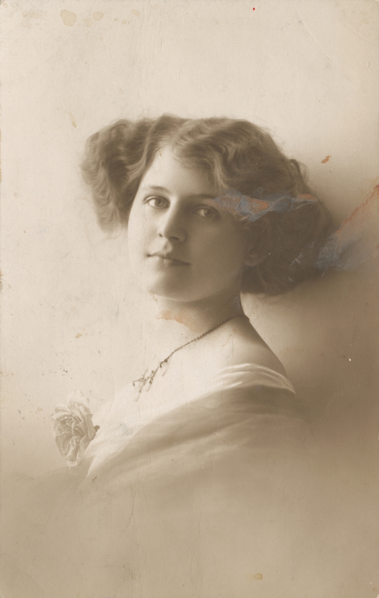 Postkortmotiv av ei ung kvinne med halskjede og rosett.