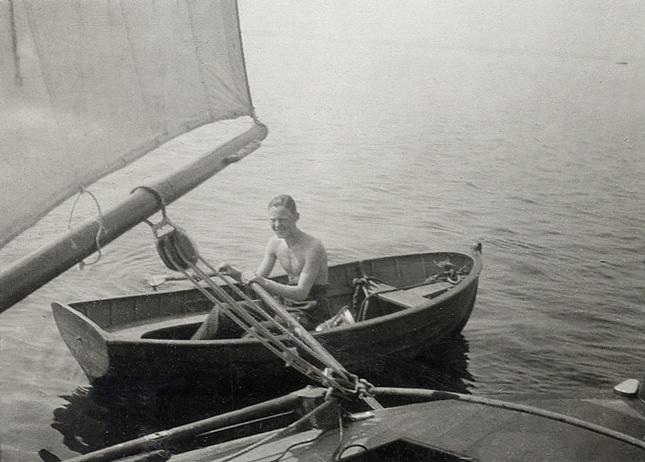 En ung man som verkar ro förbi en segelbåt i en jolle.