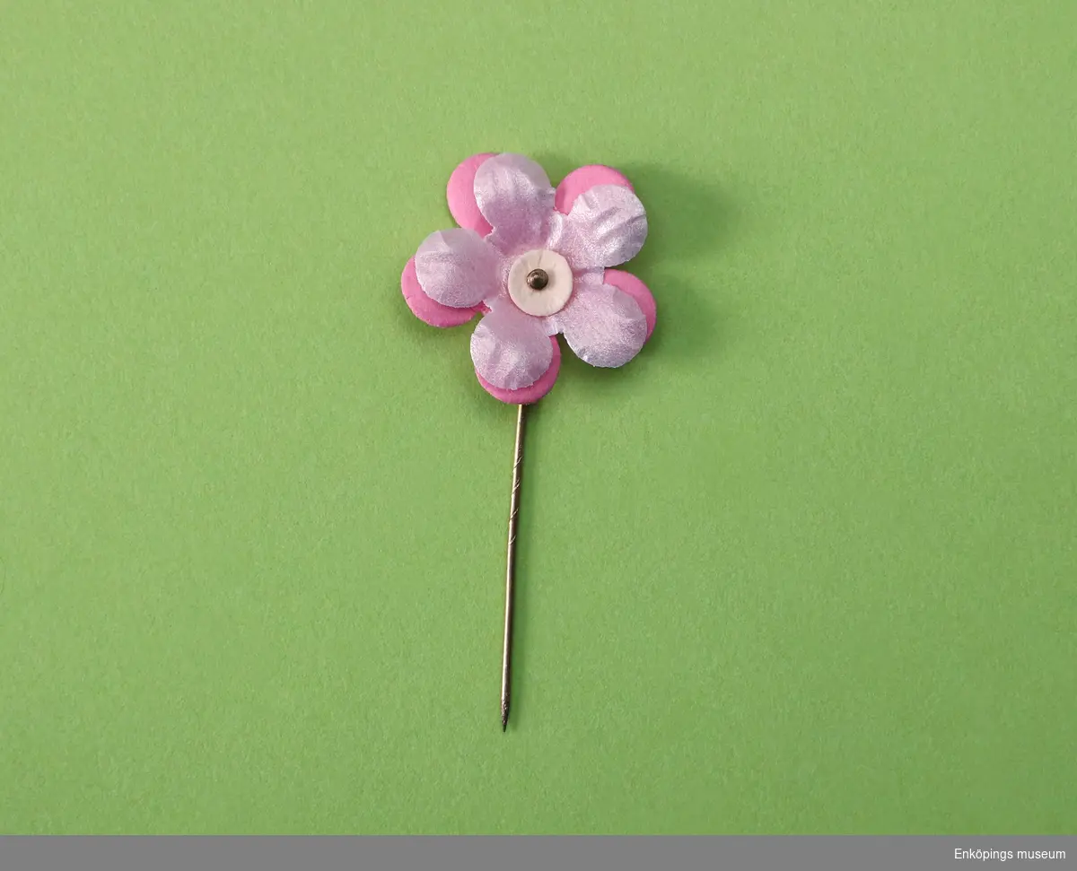 Majblomma från år 2004.
Blomman är gjord av rosa papper och celluloidblandning och har fem blad i två lager. 
Det övre lagret är ljusrosa med pärlemorskimmer och är gjort av en celluloidblandning. 
Det undre lagret är mörkare rosa och gjort av papper. 
Blomman har en vit mittknapp i papp. Det som håller blommorna samman är en nål av mässing.