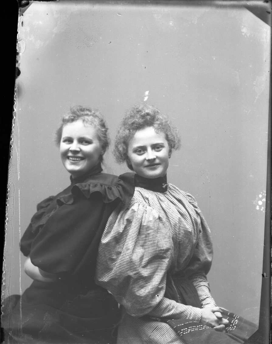 Två skrattande unga kvinnor sitter med ryggen mot varandra och blicken mot fotografen. Kvinnan till höger Ester Grönberg.