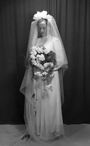 Fotografi av en brud i 0949. Bruden har lang hvit kjole, stor blomsterbukett og slør.