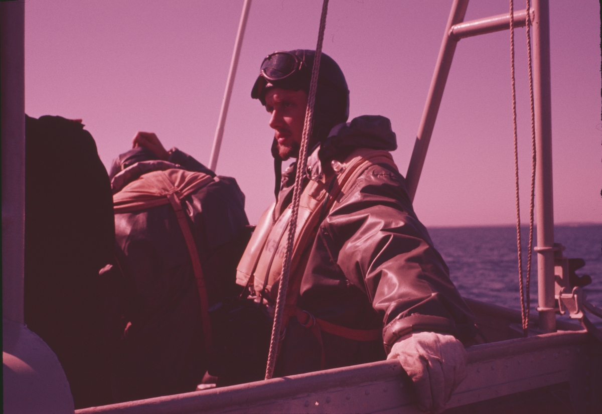 Bilden visar sjömän en sjöman med skyddskläder och flytväst ombord på ett fartyg