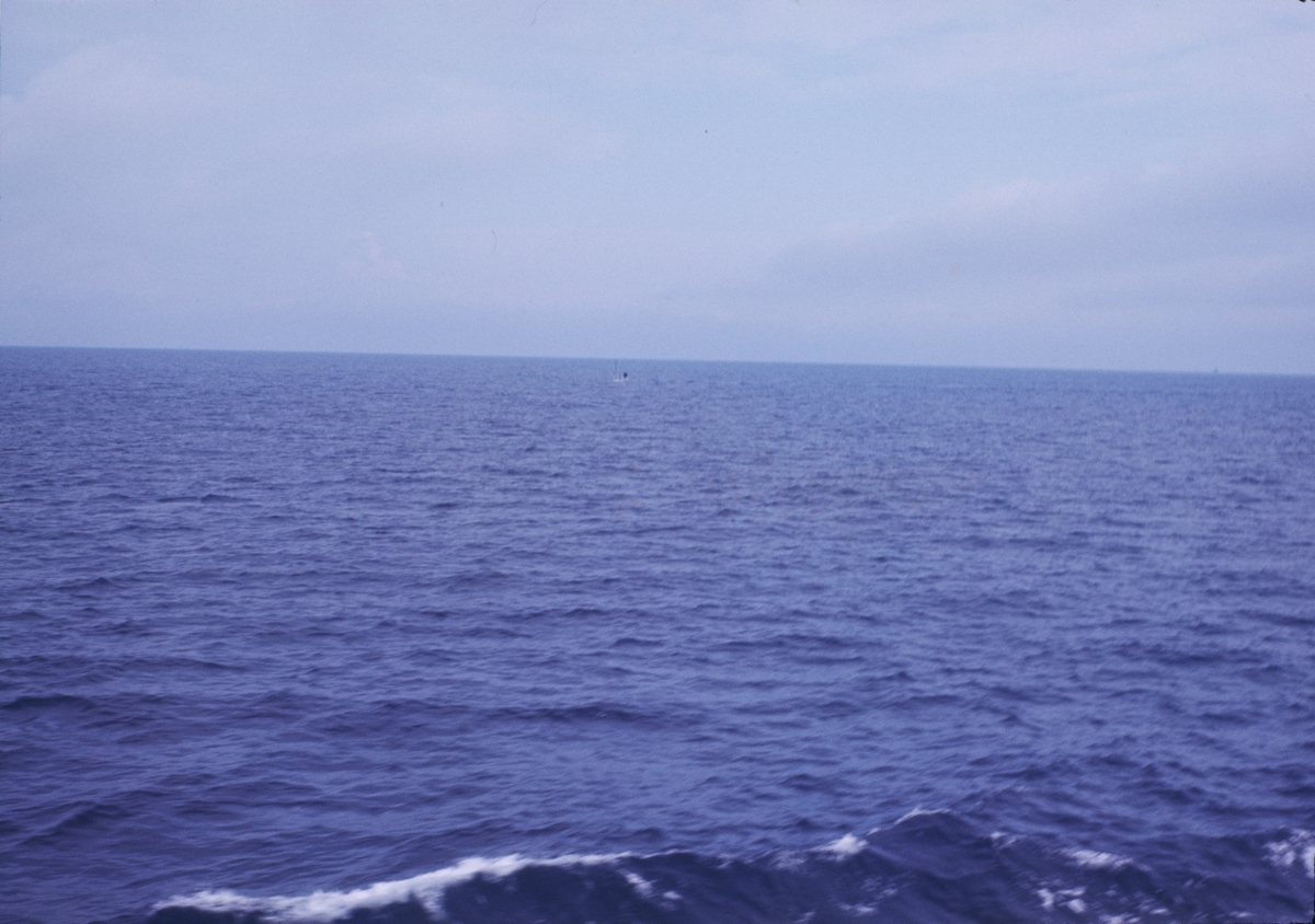 Bilden föreställer en vy över havet. I bildens centrum syns föremål som sticker upp från vattenytan. Förmodligen är det en ubåt i u-läge.