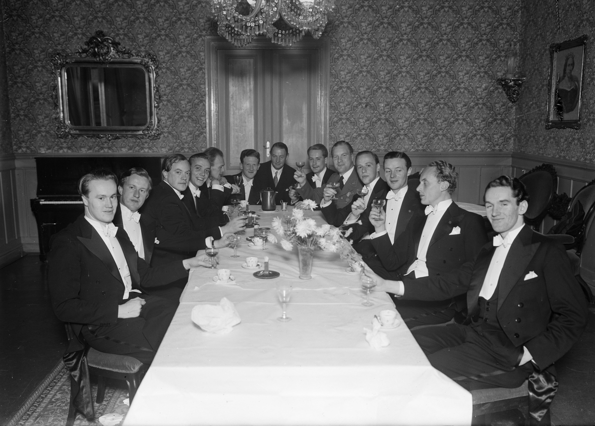 Högtidsklädda män sitter vid ett bord i en festlokal, Uppsala
