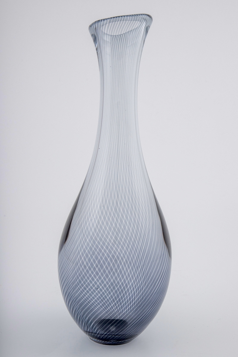 Høyreist dråpeformet vase i "Graalglas". Vasen er dekorert med spiralformede striper i underfangsteknikk, hvor det oppstår en optisk effekt i mønsteret ved å veksle mellom gråfargede og klare partier.