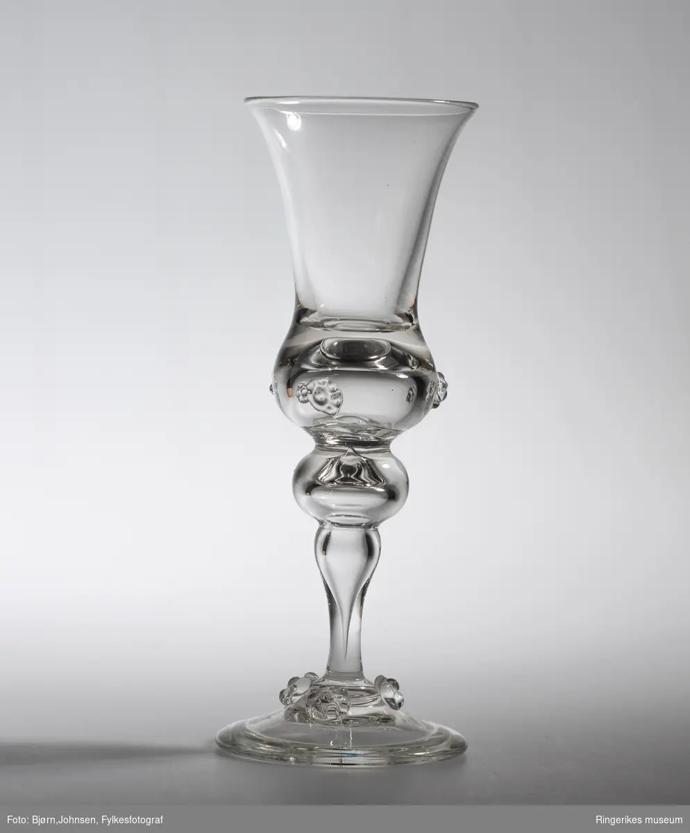 Klukk drammeglass med bringebærornamenter på både glass og stett. Fra serien Nøstetangen, produsert fra 1876 på Hadeland Glassverk.