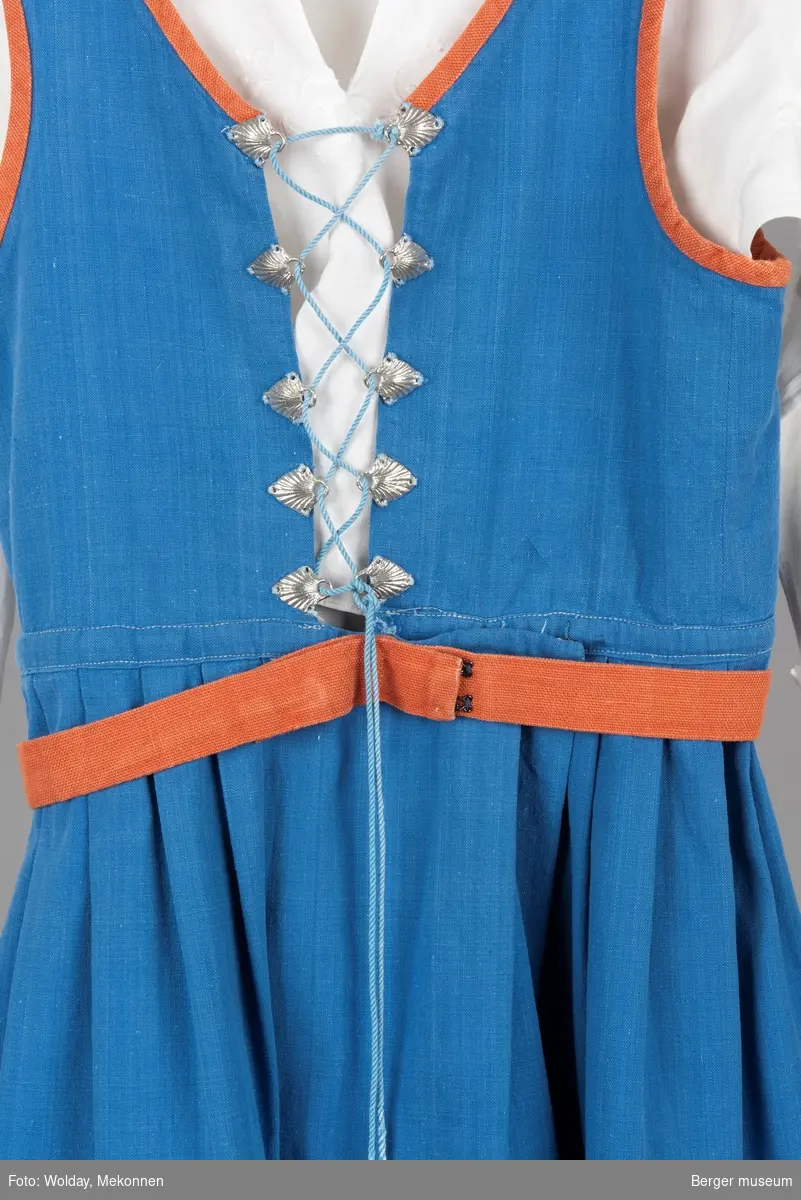 Barnebunaden/stakken er for jente i 10-12 års alderen. Den er blå med oransje detaljer, sølvhemper med skjellmønster, hvit bunadskjorte med hvite broderier. Hempene holder bryststykke sammen med en snor.