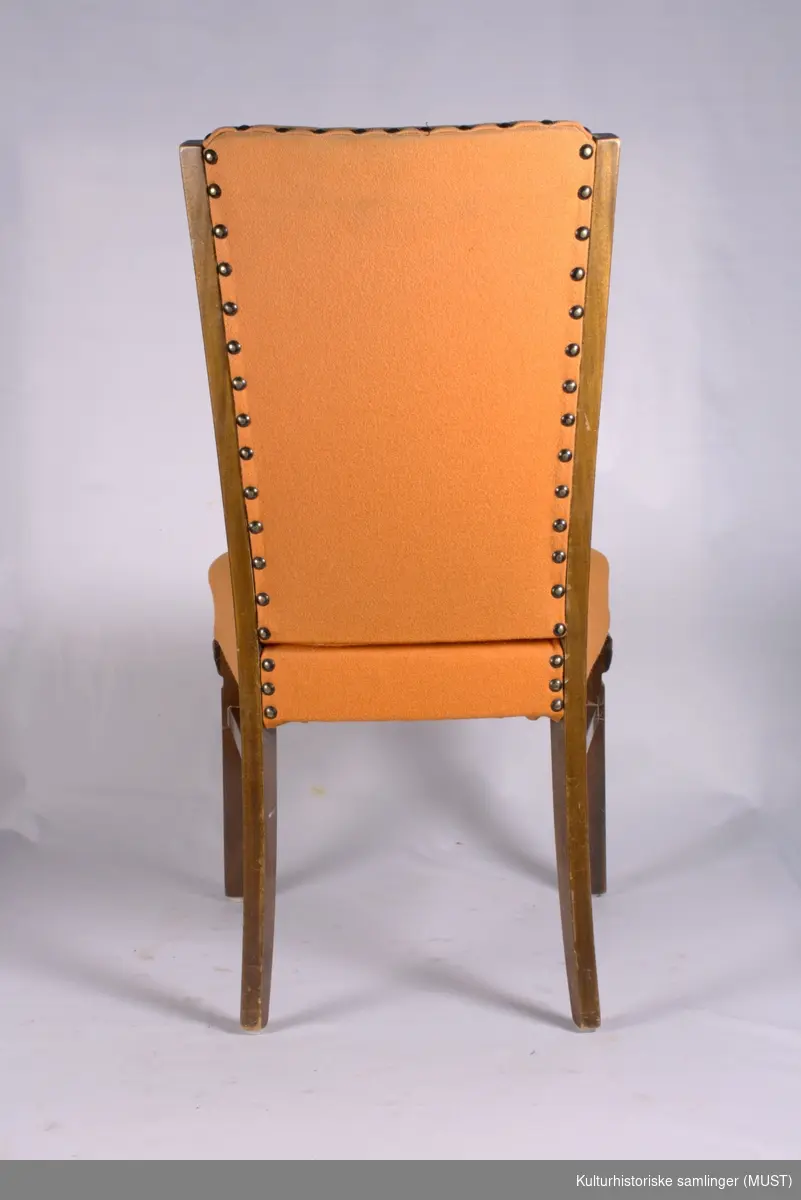 Spisestuestol med sekundært oransje trekk. Stoppet rygg og sete. Frambein formet som korintiske kapitel.