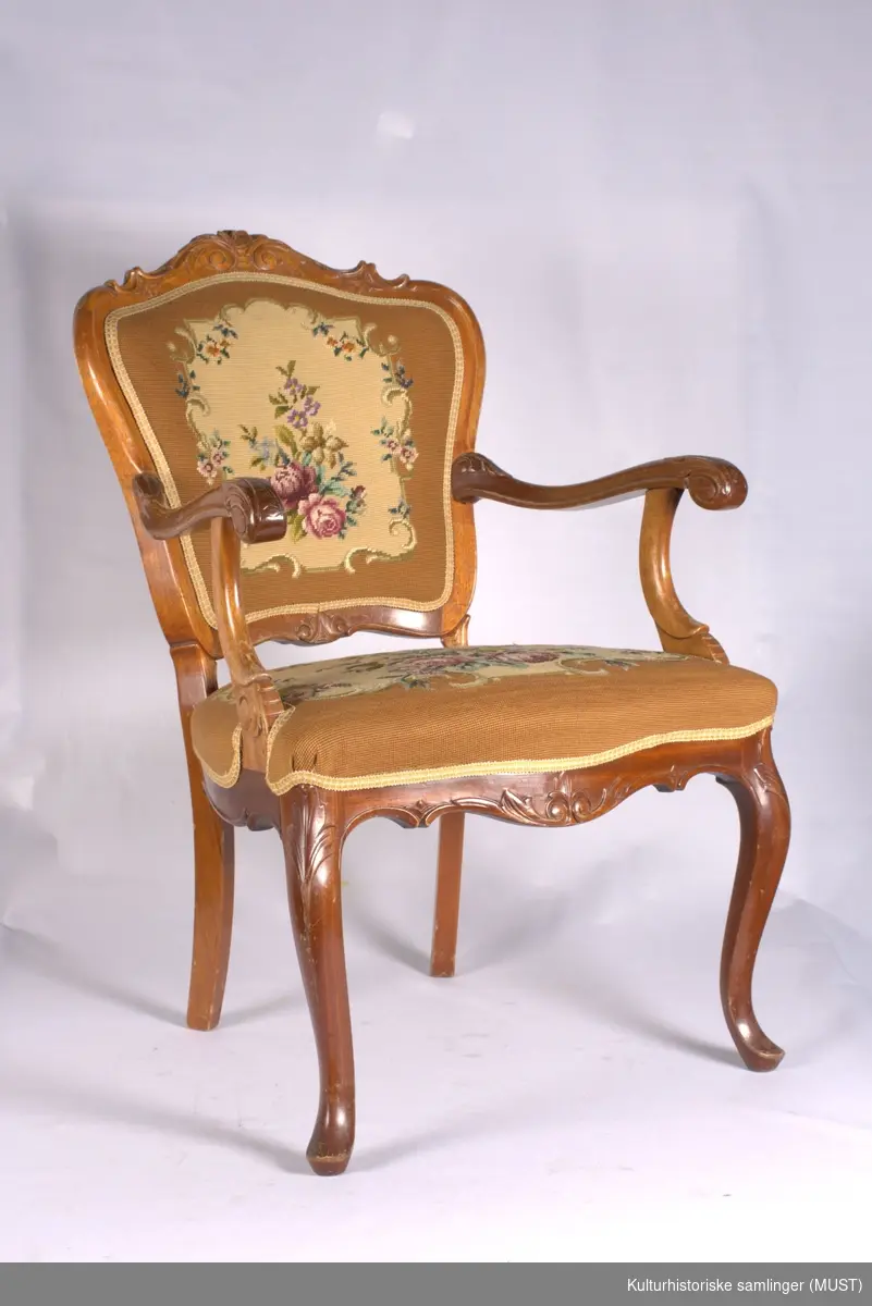Armstol av mahogny med brodert trekk på sete og rygg. Svugne armelener, og frambein. Utskåret med blomster og akantus.
