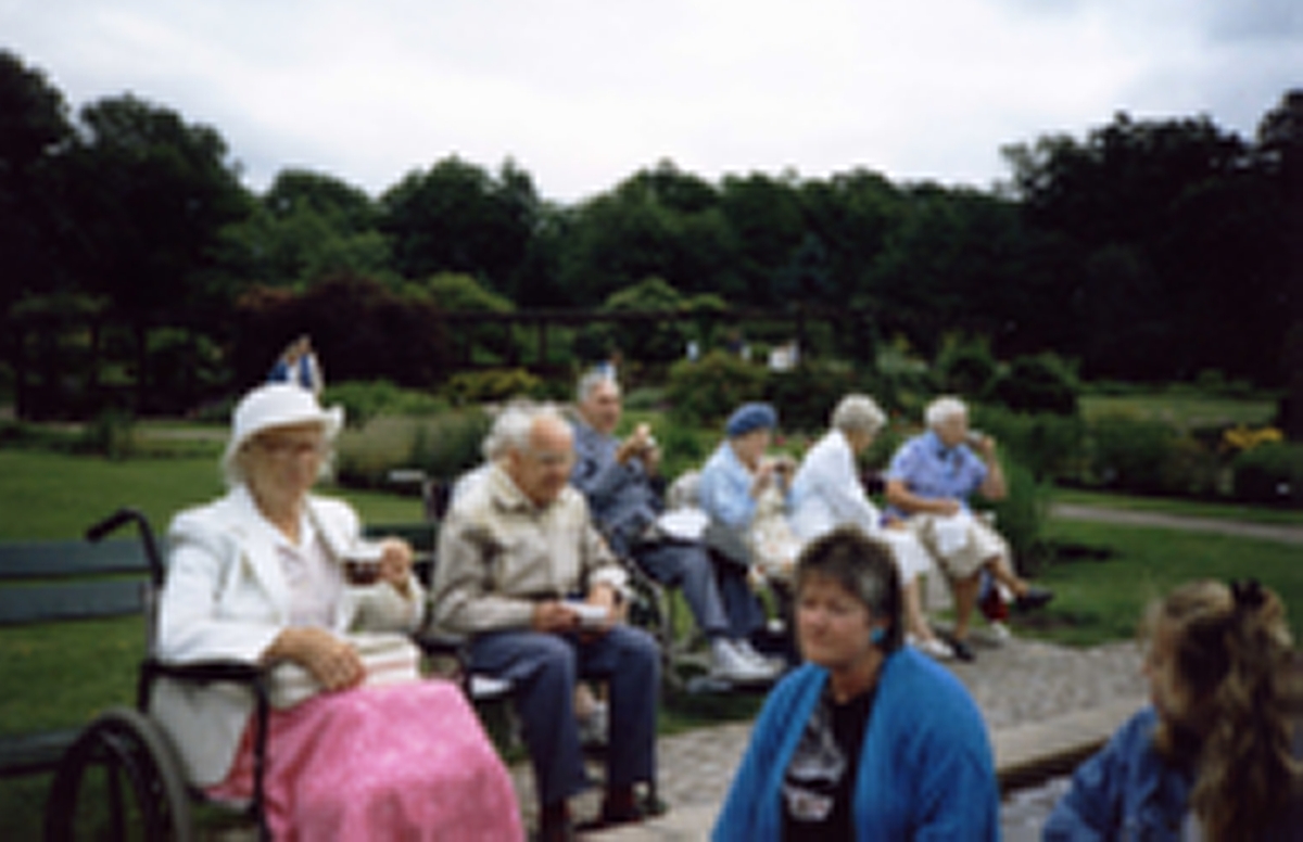 Brattåsgårdens ålderdomshem är på utflykt till Botaniska trädgården, 1980-tal. Från vänster: 1. okänd, 2. okänd, 3. Carl Eliasson (i rullstol), 4. Agnes Eliasson (blå hatt), 5. Margit Antonsson. Övriga är okända.