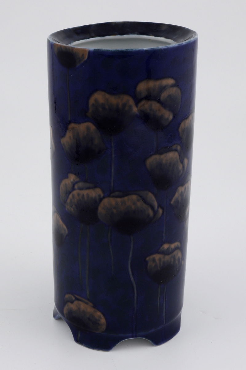 Vase i støpt porselen med underglasurmaling. Sylinderfomet korpus med konveks munningsrand. Yttersiden er dekorert med stiliserte ferskenfargede valmuer mot en mørkeblå bunn med sorte spetter. Innersiden er i hvitfarget glasert porselen. Korpus bæres av fem små ben.