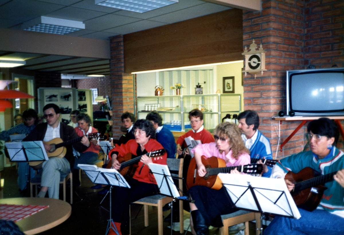 Musikskolan är på besök och spelar gitarr i Brattåsgårdens matsal på Streteredsvägen 5, cirka 1990. Musikerna består av en grupp på 11 personer.