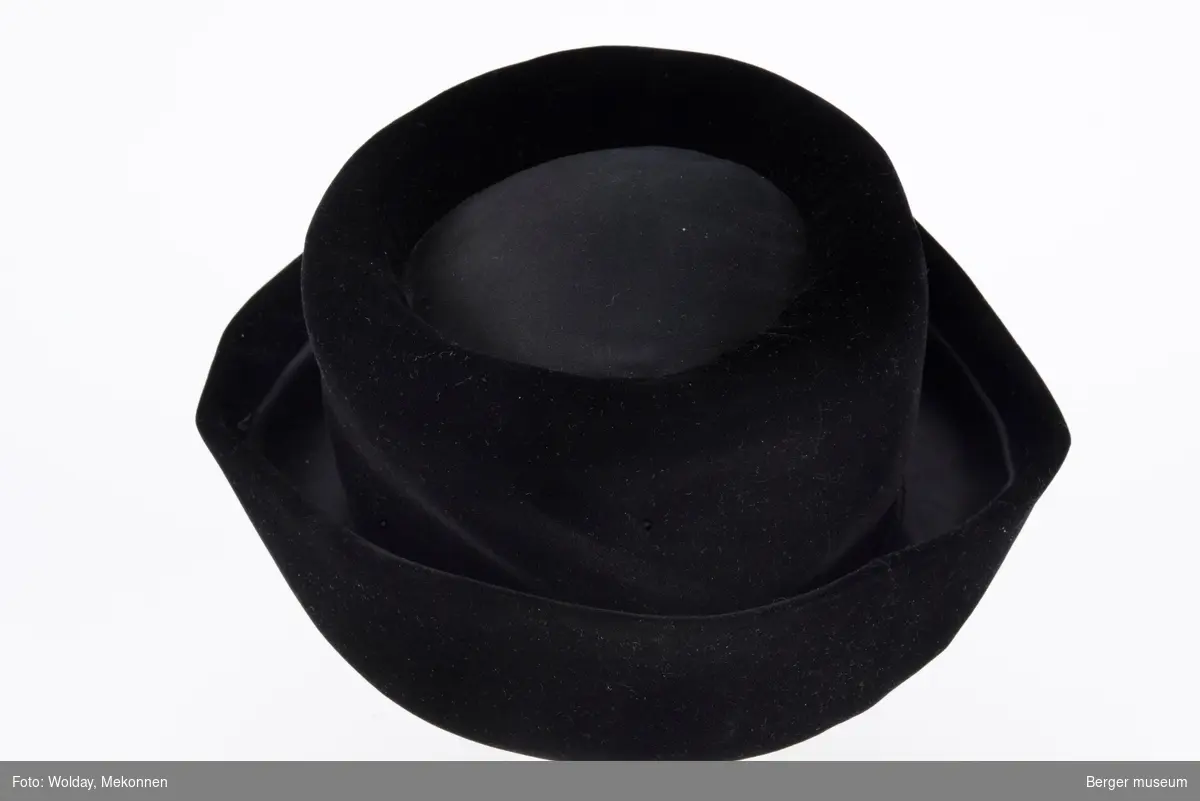 Liten svart fløyelshatt med to knapper foran til pynt. En anvennelig hatt til alle anledninger.
