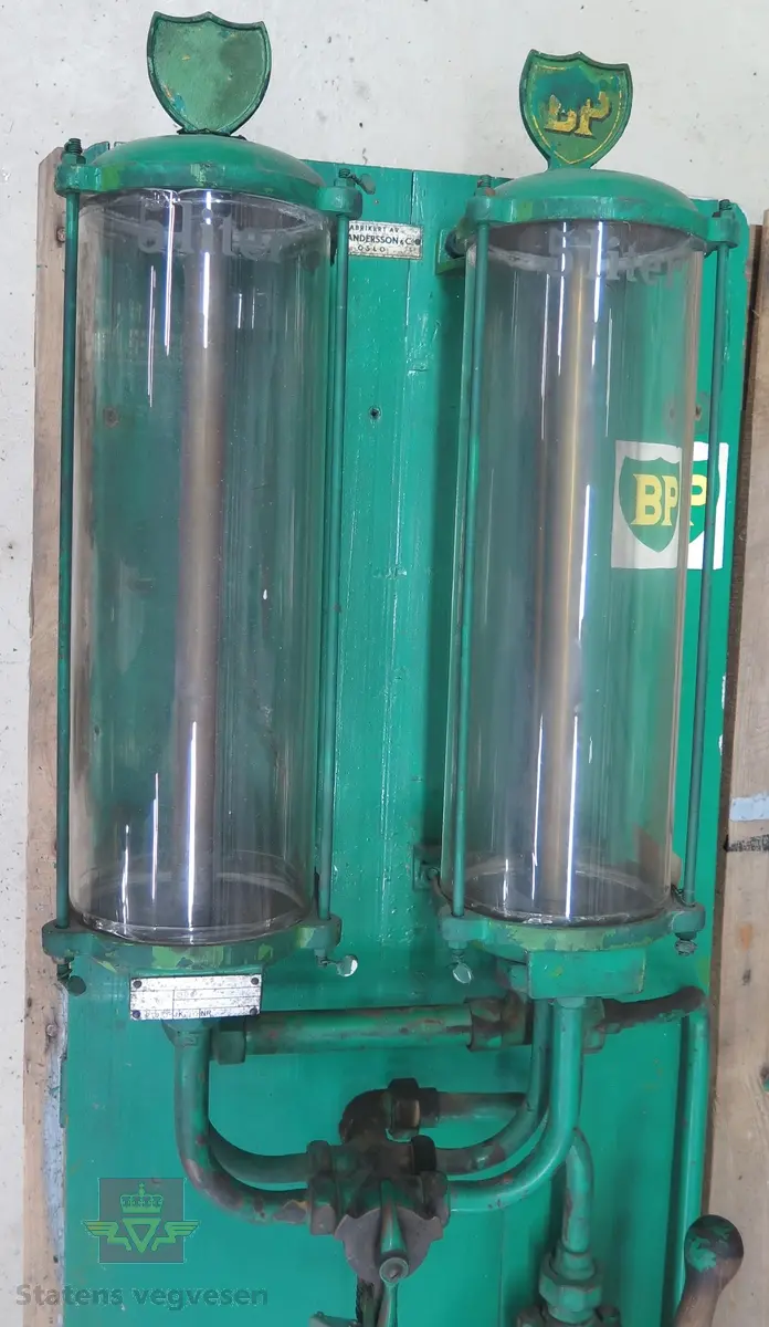 Hånddrevet pumpe med to femliters beholdere slik at man kan pumpe opp drivstoff og deretter tappe 5 eller 10 liter. Utstyret er montert på treverk Begge beholderne er plombert. Merking fra produsent og merking fra kontrollmyndighet.