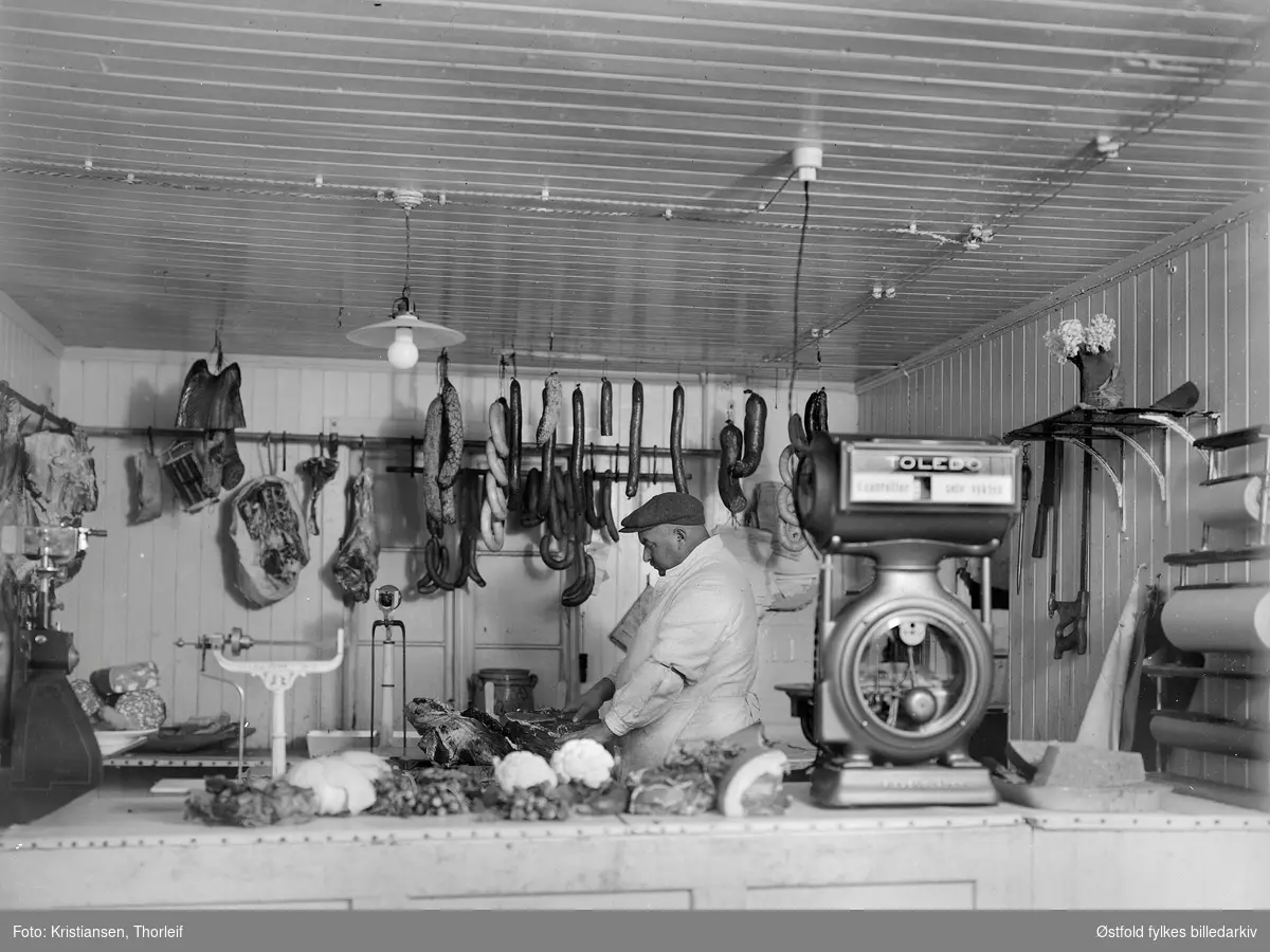 Alf Johansen Helle kom fra Fredrikstad til Spydeberg i 1922 og kjøpte Fredheim, der han startet kjøttforretning i 1923. På skiltet står det "Spydeberg kjøttforretning og Grøntsaker. Indeh. Alf Helle". Byttet seinere navn til Brødrene Helle, da de tre eldste sønnene overtok.
Alf Helle bak disken.