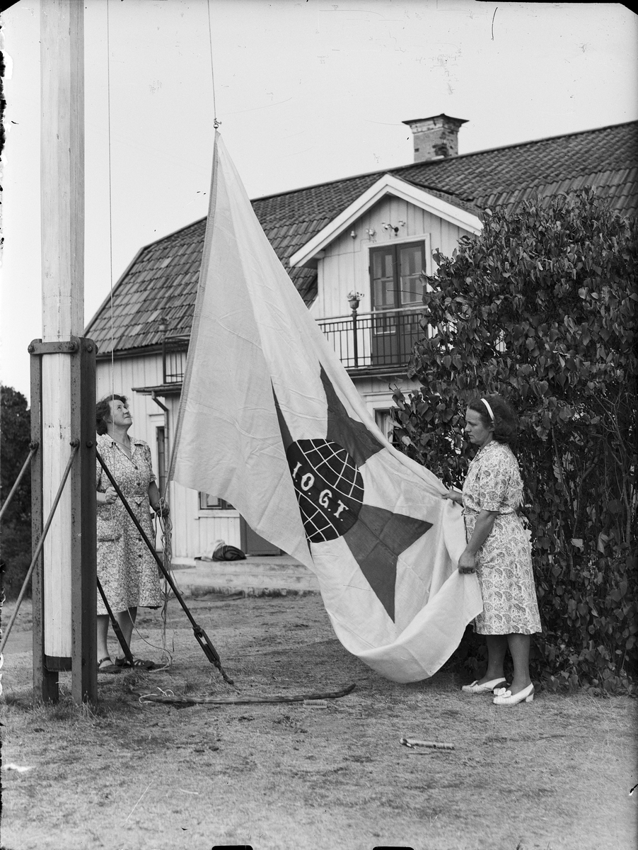 Två kvinnor hissar eller halar I.O.G.T. flagga, Sandika, Harg socken, Uppland