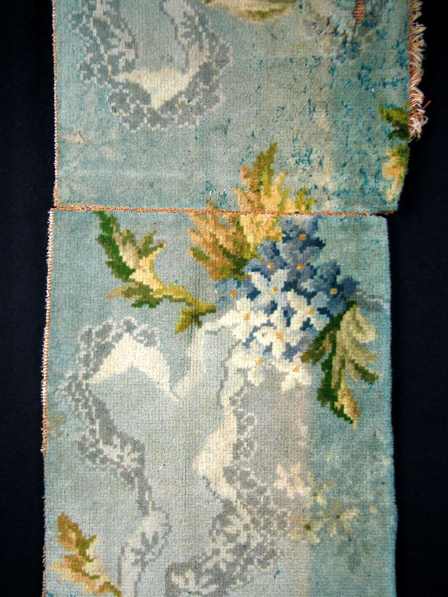Fragment av golvteppe i ullfloss. Motivet er blomster og bladverk i nyanser av blått, grønt, beige og hvitt. Skjøt. Maskintilvirket.
