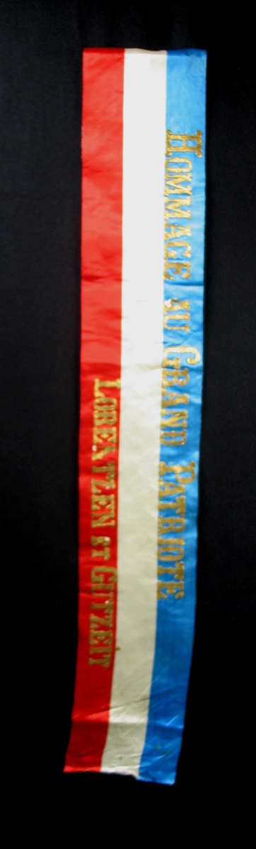 Begravelsessløyfe i rød, hvit og blå silke med skrift i gull.