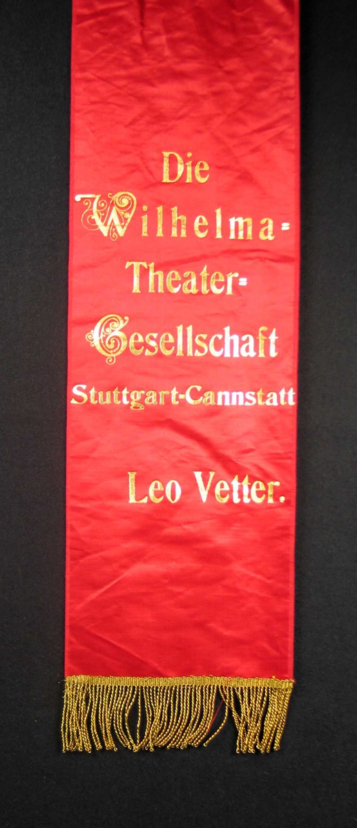 Begravelsessløyfe i rød silke med tekst og frynser i gull.