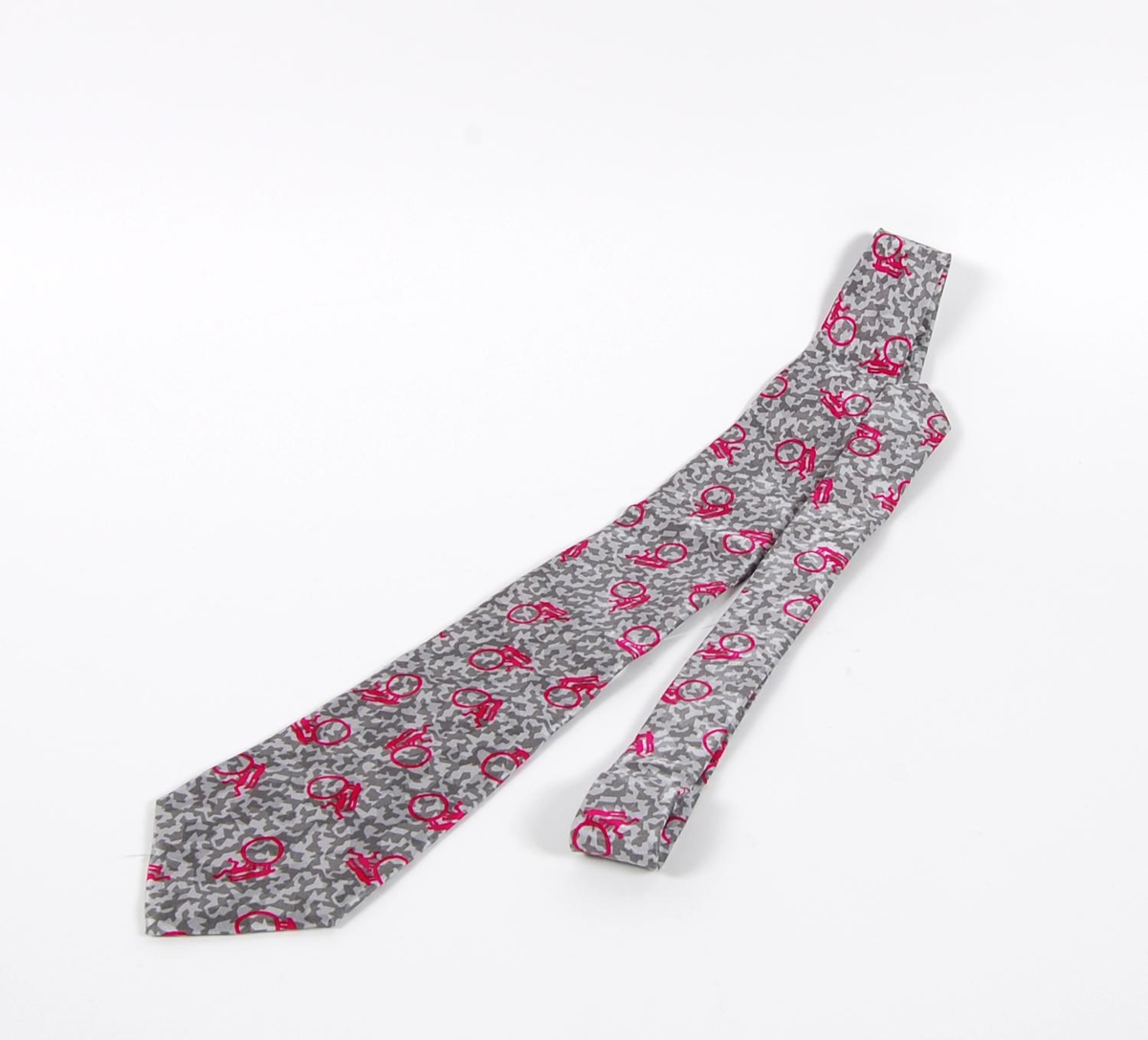 Grått slips av silke med rosa piktogrammer. Piktogrammene inngikk i LOOCs designprogram. Det er også piktogrammer på innsiden av slipset. På slipset er det påsydd merke med logo for de olympiske vinterleker på Lillehammer i 1994.