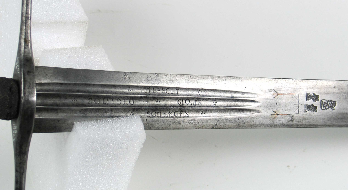 Skarprettersverd.  Pæreformet knapp med fasettetert dekor.
Tregrep viklet med rokkeskinn. 
Rette åttekantede parérstenger som ender i to dråper med kantet dekor. Rett tveegget klinge med ovalt tverrsnitt  og tre korte blodrender på hver side. Innslått tre smedstempler med kronede hoder.  På den ene siden er det gravert inn et hjul og på den andre siden en galge. Begge inngraveringer er innlagt med kobber.

