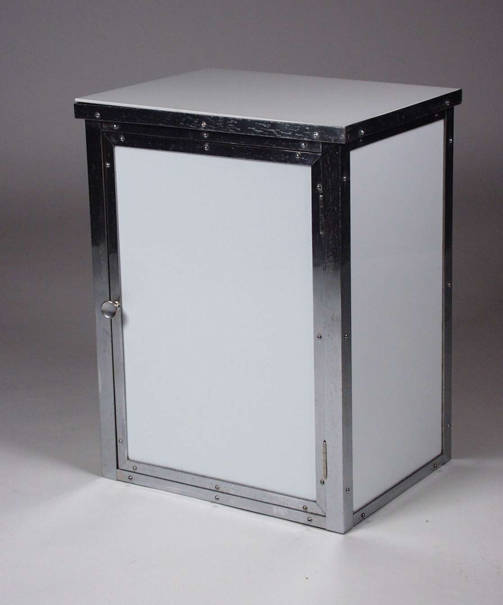 Skap i tre dekket med hvite glassplater. Skapet er kantet med metallister. Det har to hyller i glass innvendig. 