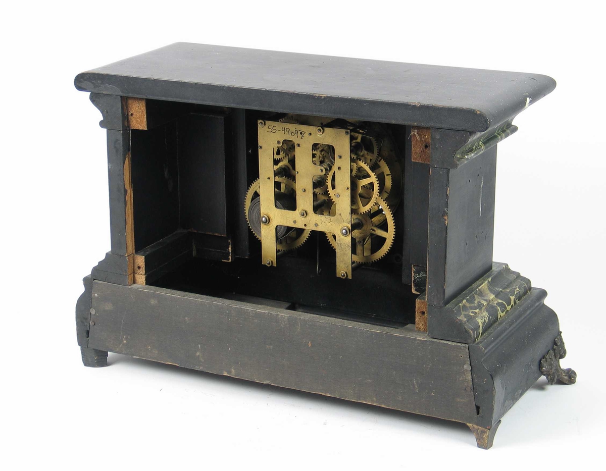 Klokkekasse med kvadratisk midtfelt med rund tallskive, inntrukte sidefelter med opprinnelig to halvsøyler på hver side, de ytterste senere fjernet. Topplate med avrundet kant, profilert sokkel og på hørnene påsatt mønstrede messingbein. Svartmalt og litt bruk av grønn marmorering. Topplaten er flat, og har gitt plass til eventuelle løse figurer på toppen. På sidene av klokkekassen har det også vært dekorative messingornamenter.