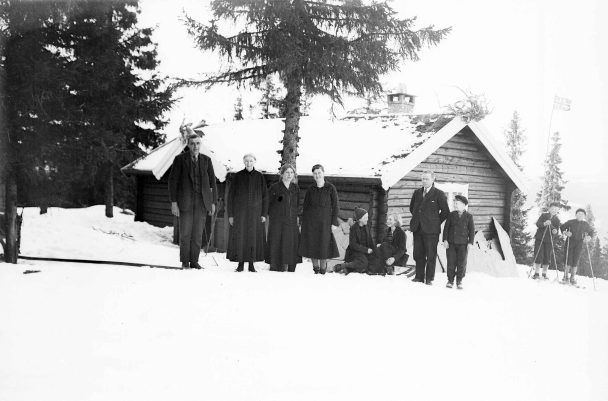 Gruppe med menn og kvinner foran hytte kalt "Høgly" på Bakkestulen, eid av Øyvind og Mina Berge, vinter 1934.