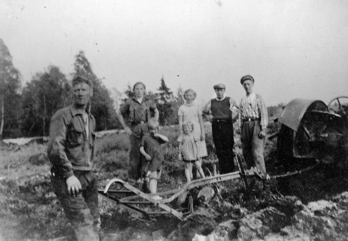 Gustav Lange med plogenetter traktoren. Lengst til høyre broren Odd. Kvinner, barn og arbeidskarer seg på.