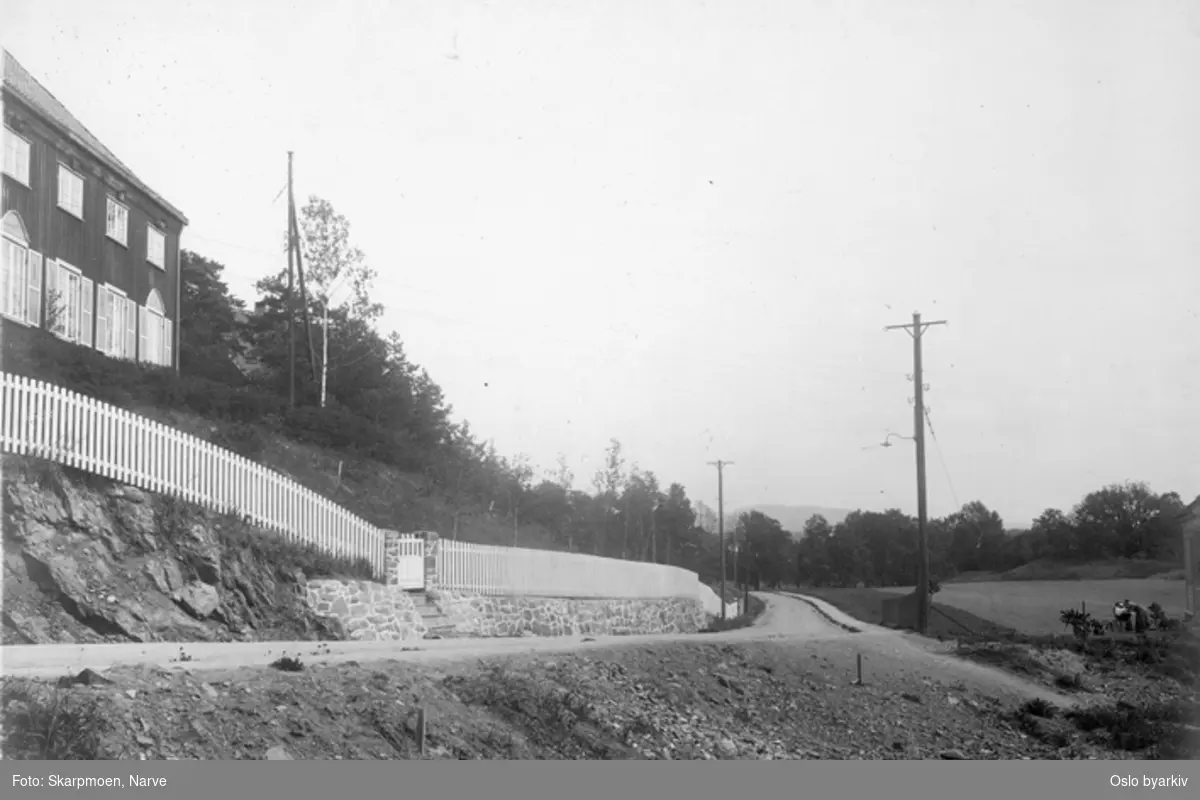 Trevilla bak hvit stakitt til venstre, grusvei, kvinne med barnevogn til høyre, bildet tatt i forbindelse med utbyggingen av Lilleakerbanen som ble åpnet 1919