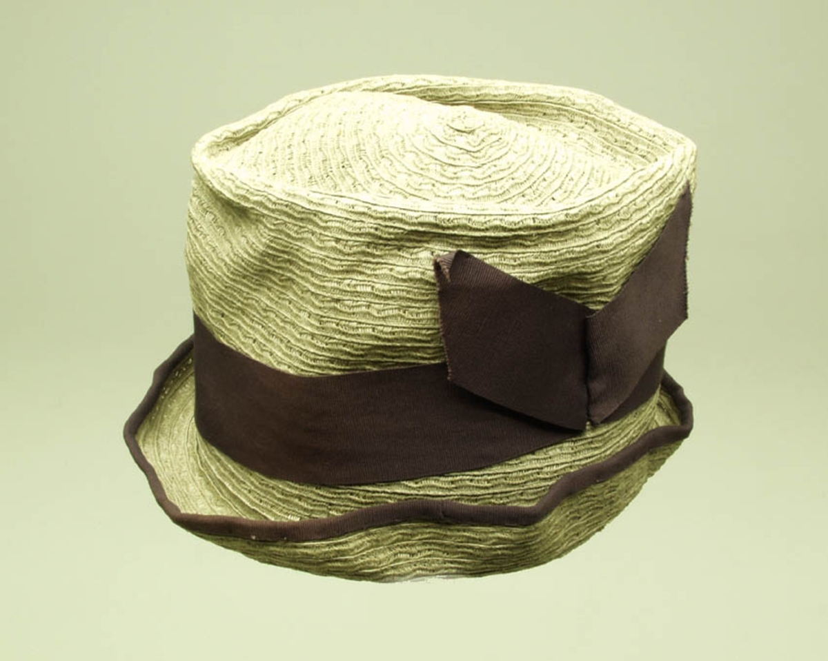 Hatten er sydd sammen av bånd. Bøttehatt. Den har fiolett ripsbånd, 4, 5 cm. bredt, smal kant ytterst. Silke fòret innvendig er stivet opp med sponbånd i overgangen hatt/bunn. 