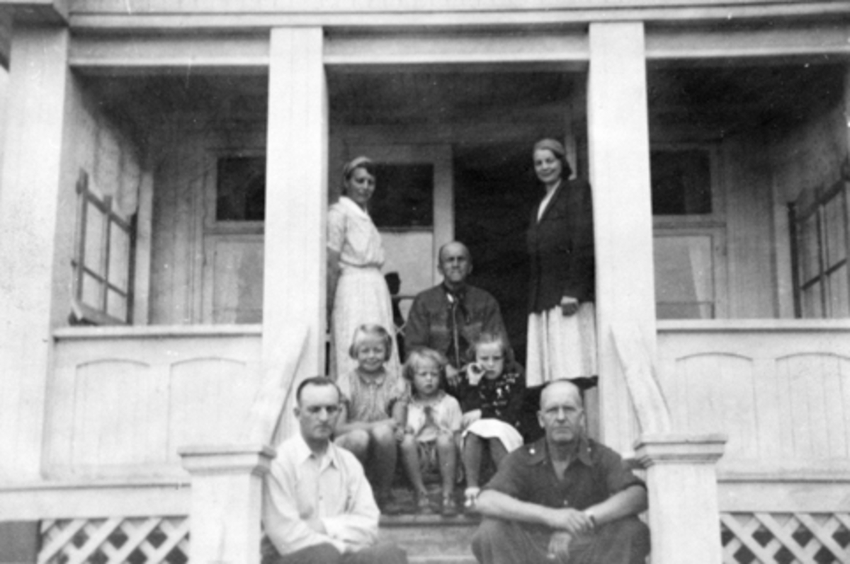 Familien Helgeby samlet på veranda på Sandvold, Nes, Hedmark. Fra venstre er Marie (1902-1979), Aslaug (1898-1977), Einar (1866-1948), Asbjørg Margrethe (1937-1998), Solveig (1944-1991), ?, Håkon (1906-1988), gjest.