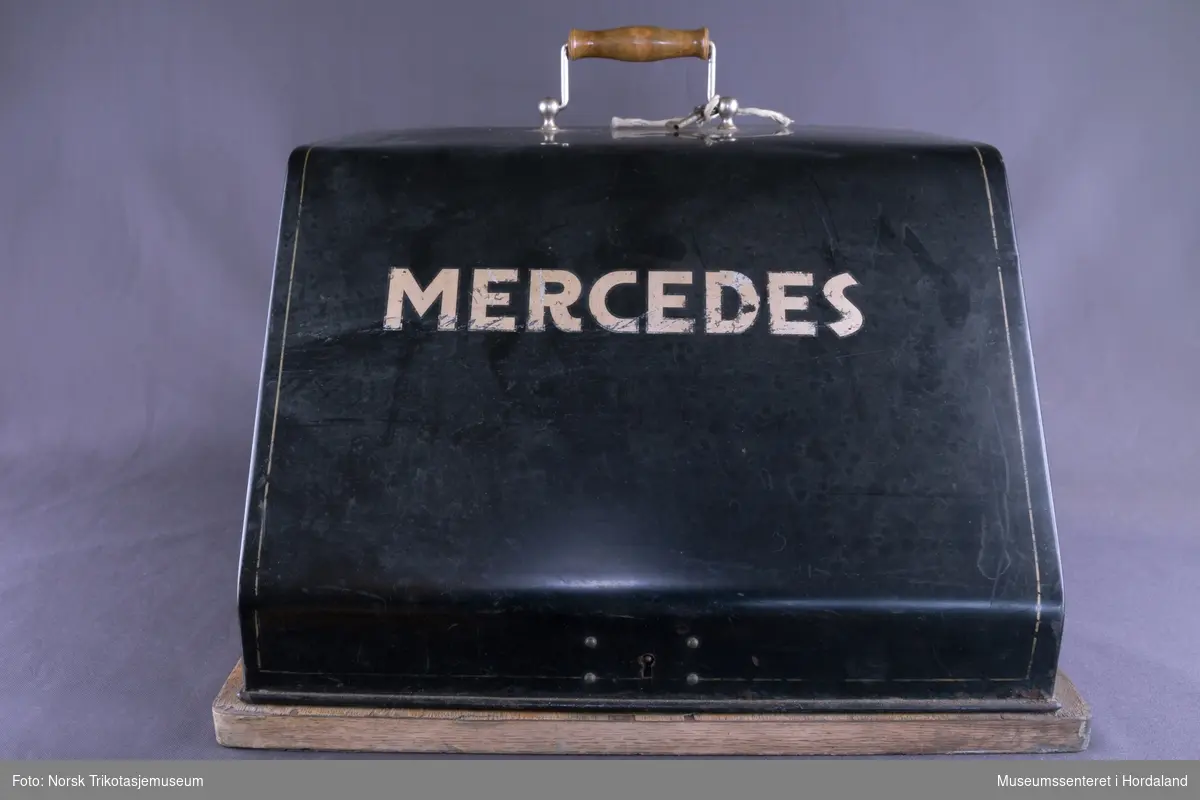 Mercedes standard skrivemaskin med gammelt tastatur, men utan bokstaven "å". Pica skrift, 9-tommers valse (kan kun skrive A4). Skrudd fast på treunderlag og har medfølgjande metallokk: ei transportabel standardmaskin.