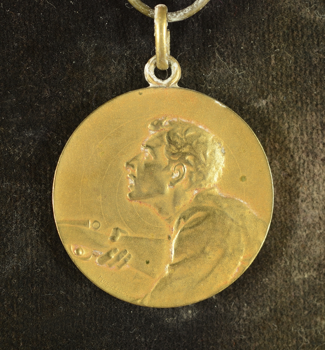 Overkroppen av en person med børse i hånden på framsiden av medaljen.
Bladkrans rundt en inngravert tekst på baksiden av medaljen.
