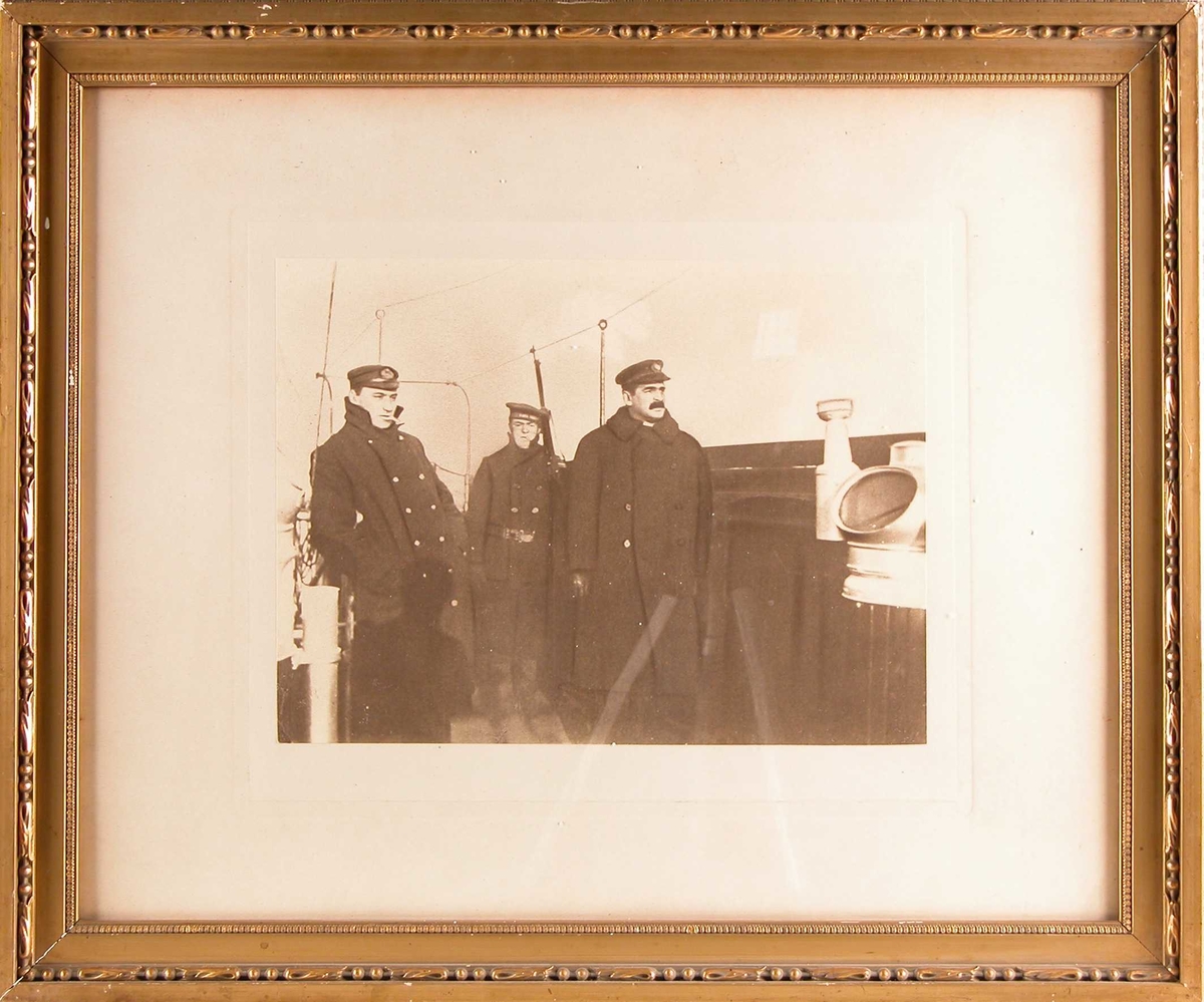 Tre menn i uniform står på skipsdekket ved siden av natthuset.