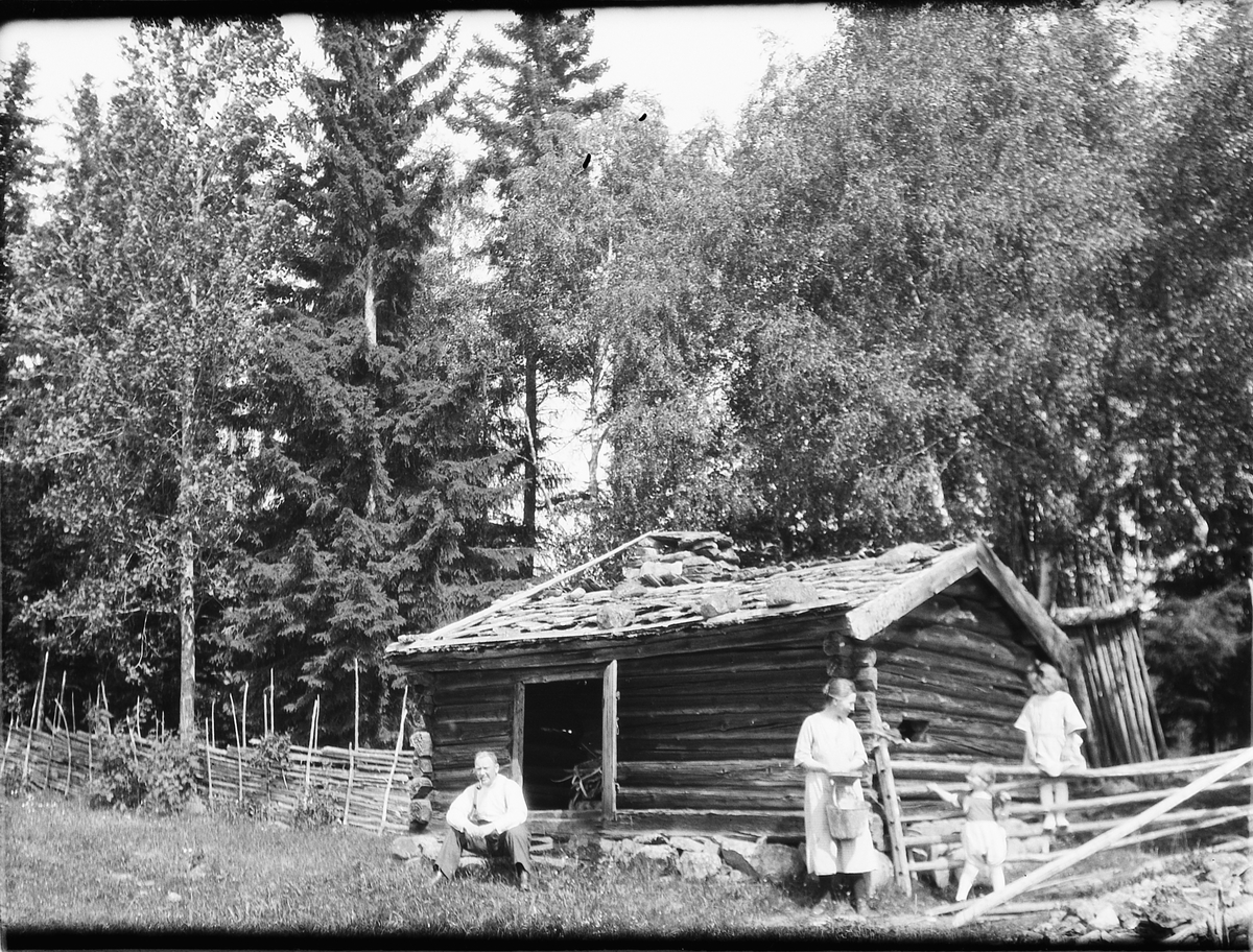 Ukjent mann, kvinne og to barn ved ei tømmerhytte i skogen. 