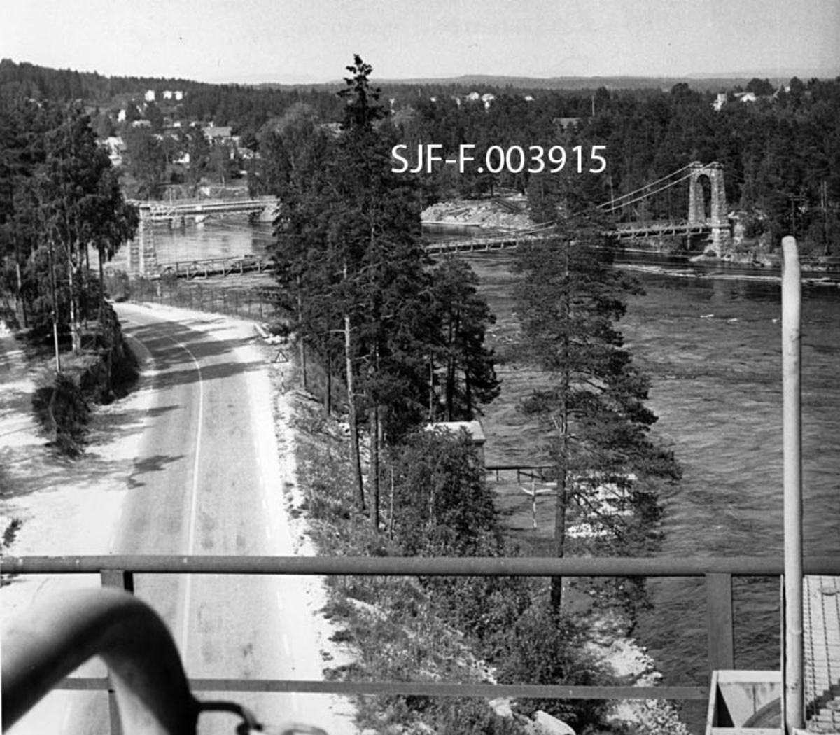 Utsikt fra kranbanen til Geithus Bruk på Modum sommeren 1967.  I forgrunnen ser vi en del av Drammenselva og av fylkesvegen mellom Geithus og Vassbunn.  Vi ser også to bruer som krysser elveløpet.  Nærmest ser vi hengebrua ”Geithus bru” – også kalt ”Nybrua” – og nedenfor jernbanebrua for sidesporet mellom Drammenselvens Papirfabrikker og Geithus stasjon på Randsfjordbanen.  I bakgrunnen ser vi deler av bebyggelsen på tettstedet Geithus. 

Baksida av den kopien av fotografiet Norsk Skogmuseum har overtatt fra Drammenselvens Papirfabrikker har følgende blyanttekst:

"Utsikt fra renseriet Geithus Bruk juni 1967. Tatt mot vest.  Vi ser Geithus og i forgrunnen hovedveg mellom Åmot og Geithus, samt i bakgrunnen dambroen ved Dr. elvens Papirfabrikker.  O. Jørgensen. "

Lokalkjente folk har påpekt at det ikke dreier seg om en "hovedveg", men en fylkesveg, og at den ikke går mellom Åmot og Geithus, men mellom Geithus og Vassbunn. 