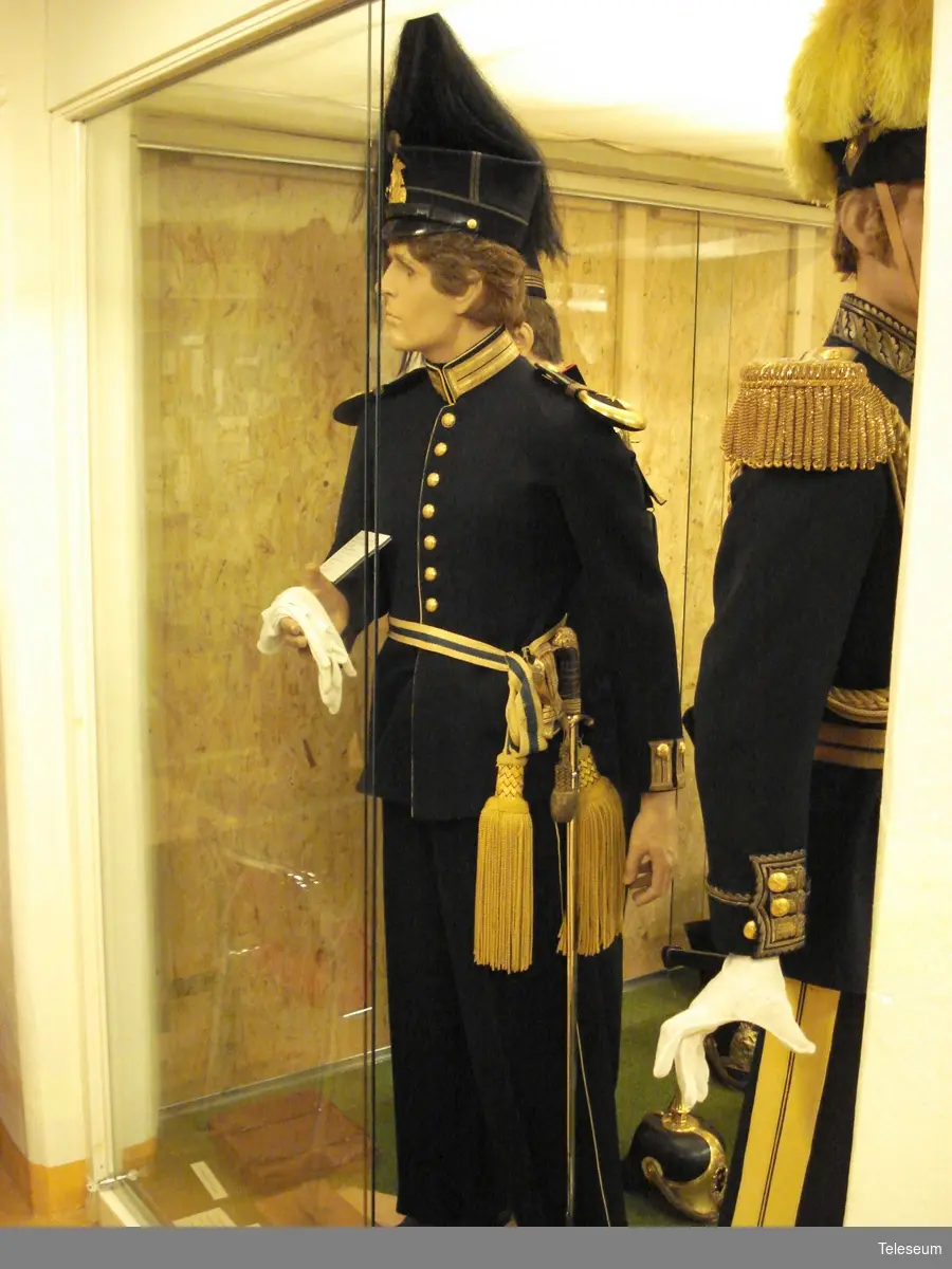Underlöjtnant vid Upplands Regemente, klädd för parad.
Uniformen består av:
Skärp m/1819-1829
Mössa m/1865-1899 med vapenplåt m/1865 och pampong m/1865-1908
Plym m/1865