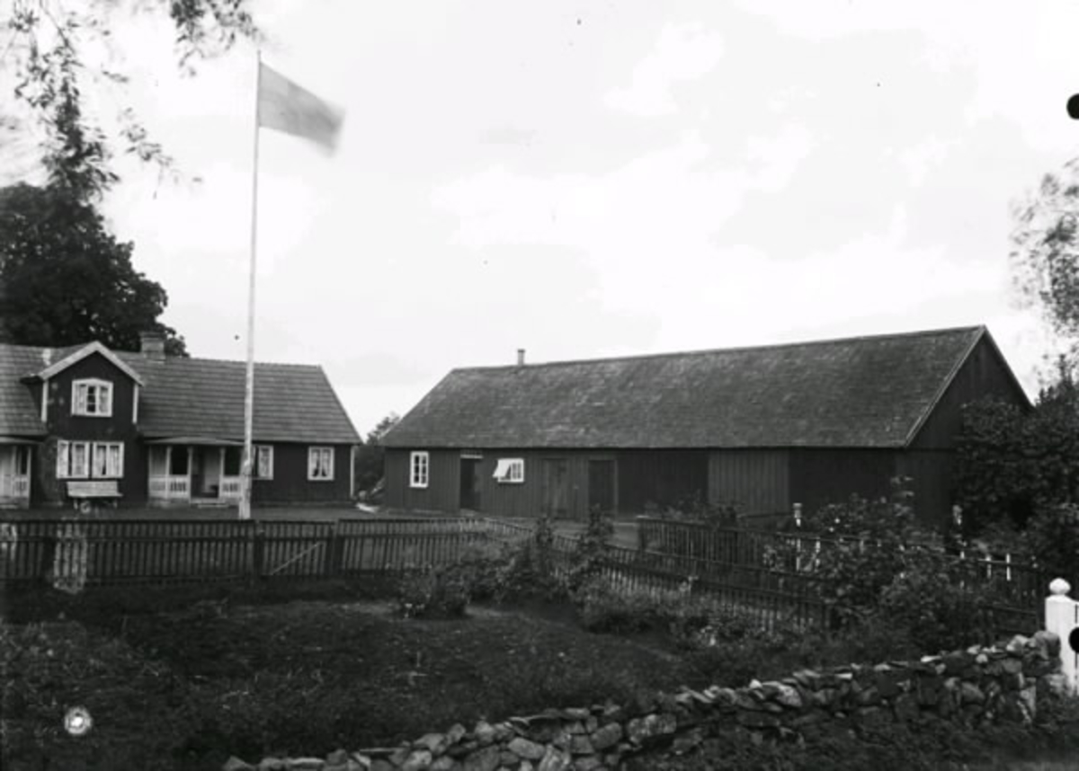 Bondgård, Elmö, i  Drängsered socken.  Mangårdsbyggnad och ekonomibyggnad. Framför boningshuset står en flaggstång med flagga. Närmast kameran en täppa som är inhägnad av en stengärdsgård och ett trästaket.