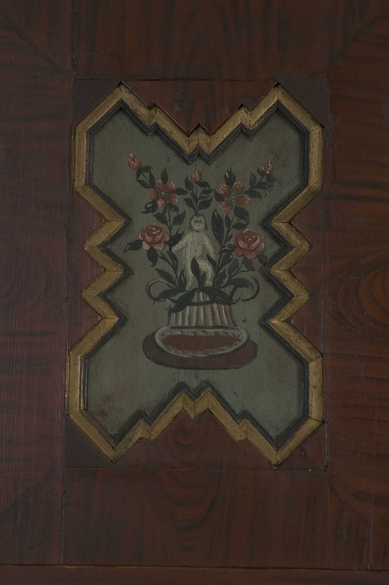 Doble dører oppe, to skyvedører på midten, en dør nede og to skuffer. Malte moriver: to adelsmenn og to blomster med nakne figurer oppi. Samson og løven på nedre skapdør. Marmorering i nisjen. Skyvedørene er dekorert med hester, kuer og geiter samt hus og en kirke.