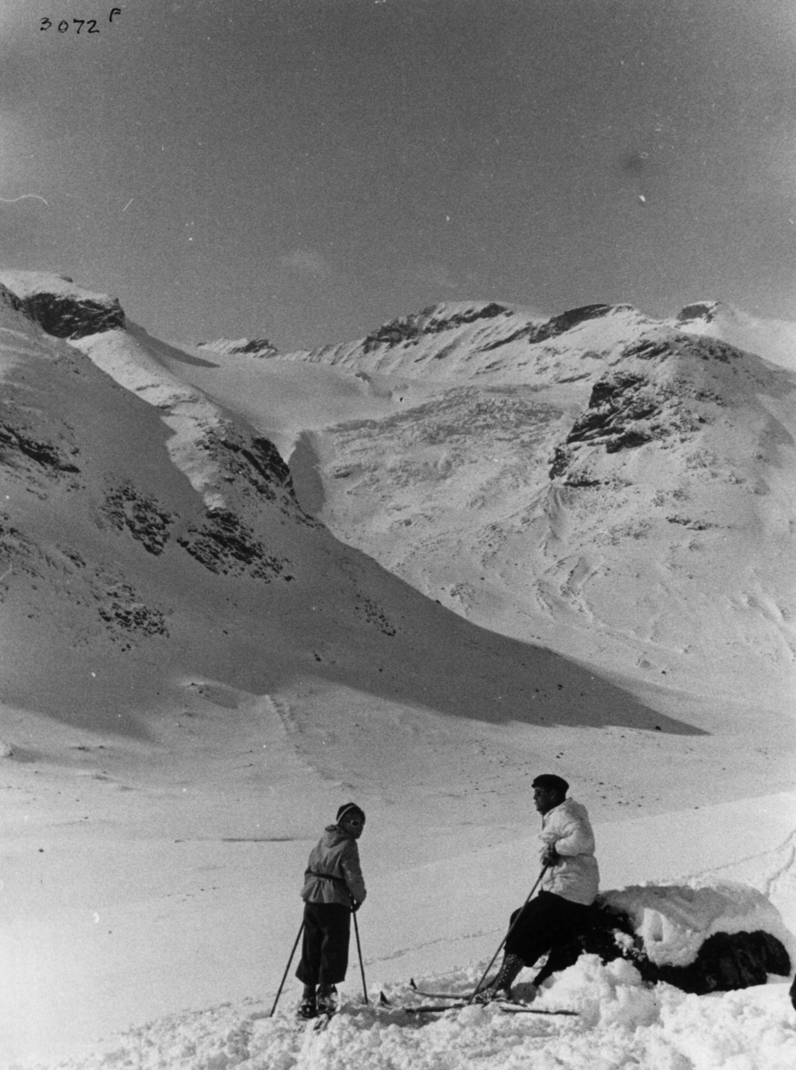 Skiløpere ved Galdhøpiggen i Jotunheimen med snødekte fjell og sol.