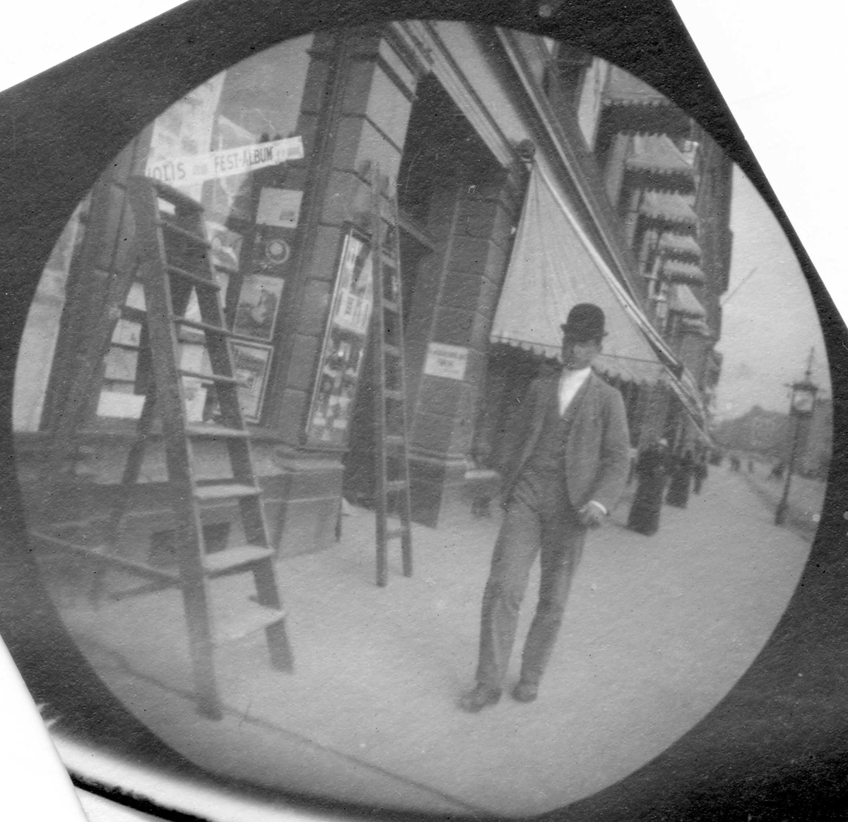 Thorvald Astrup spaserer på fortau langs butikker, Oslo. Markiser over